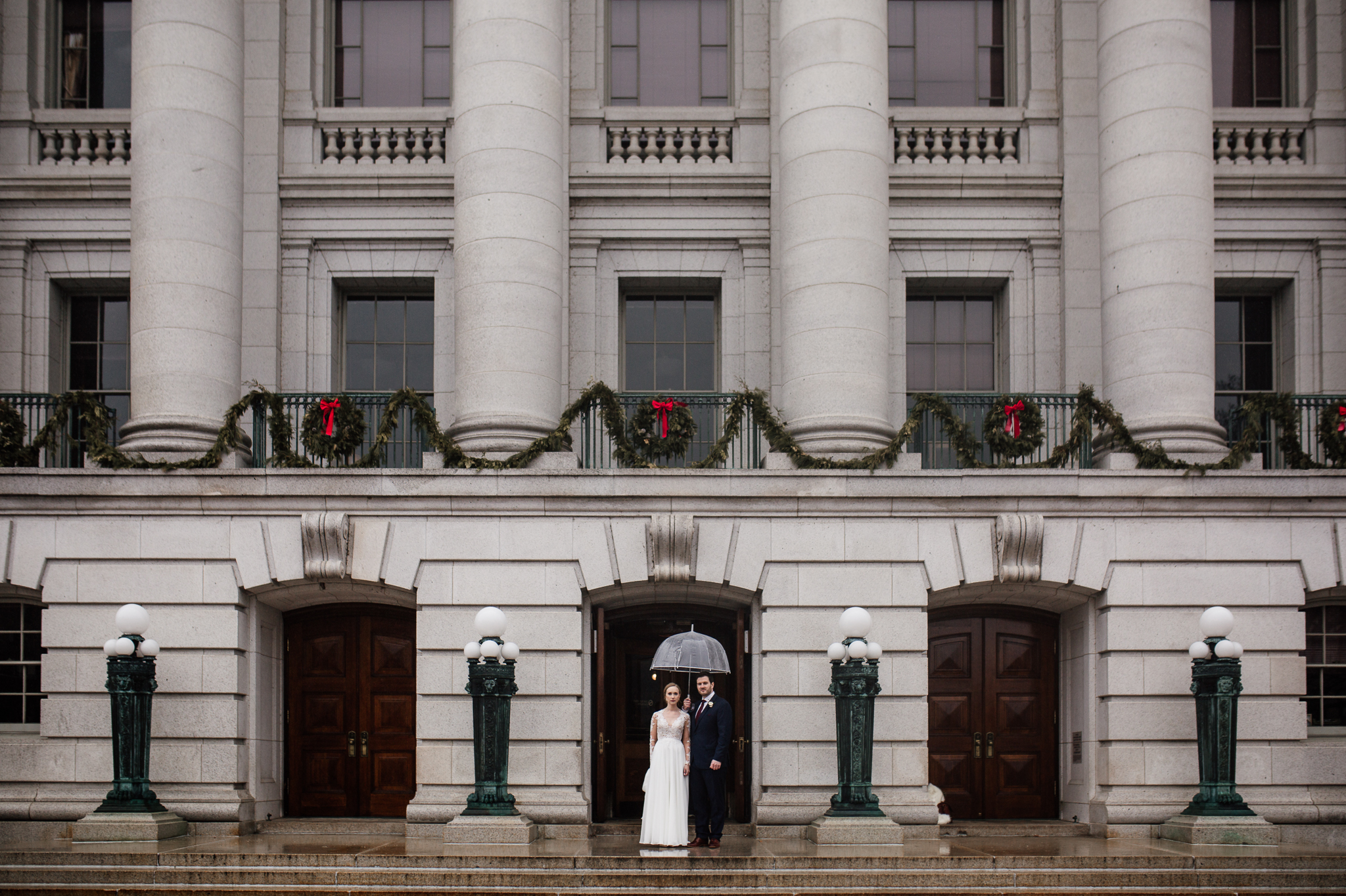 Bride and groom standing with an umbrella in the doorway of the Madison State Capitol before their Micro Wedding.